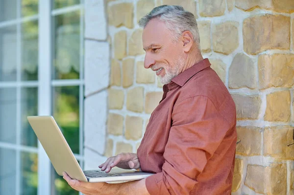 Mature man in casual clothes with a laptop near a brick wall — стоковое фото