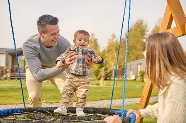 Man putting joyful kid on swing and watching woman — 스톡 사진