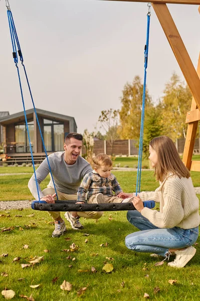 Man and woman crouched touching swing with baby — Foto de Stock