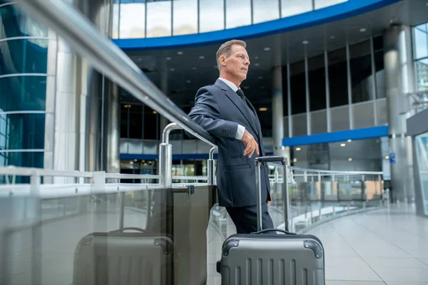 Tranquil pensive businessman with the suitcase standing at airport terminal — Stockfoto