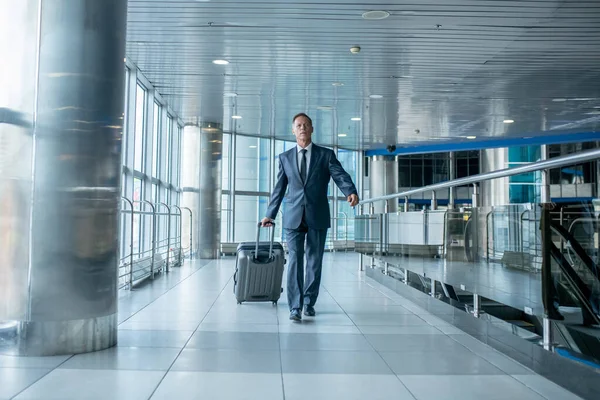 Male passenger wheeling his luggage through the airport terminal — ストック写真