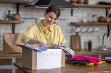 Cheerful young woman packing things for donation