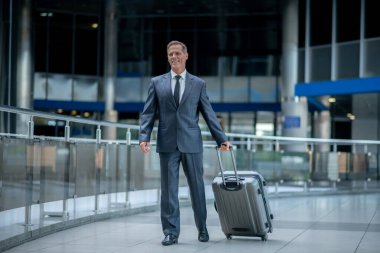 Smiling entrepreneur with his baggage walking along the airport terminal