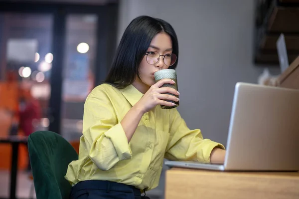 Cute asian young woman in eyeglasses at the laptop having coffee — Stock Fotó