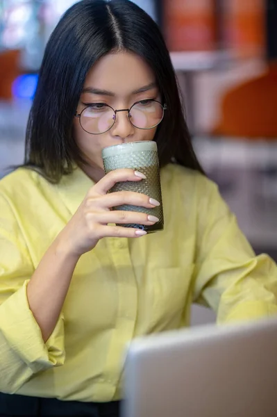 Cute asian young woman in eyeglasses at the laptop having coffee — Stock Fotó