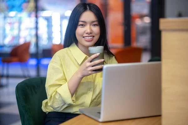 Pretty young asian woman in yellow shirt working on a laptop — Stock Fotó