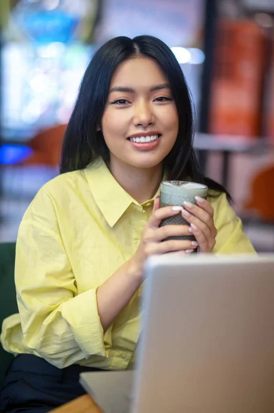 Pretty young asian woman in yellow shirt working on a laptop — Stock Fotó