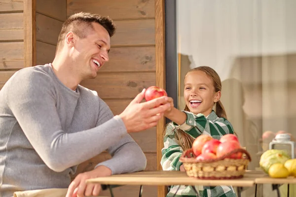 Girl treating apple to man sitting at table — Fotografia de Stock