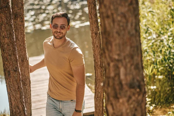 A young man in sunglasses in the forest near the river — Stockfoto