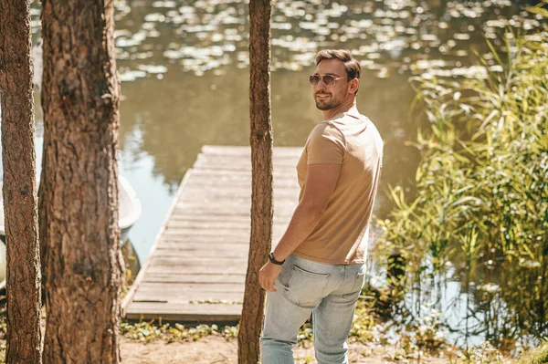 A young man in sunglasses in the forest near the river — Stockfoto