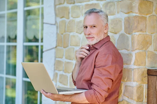 Mature man in casual clothes with a laptop near a brick wall —  Fotos de Stock