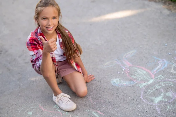 Pleased beautiful girl approving her chalk drawings on the ground — 图库照片