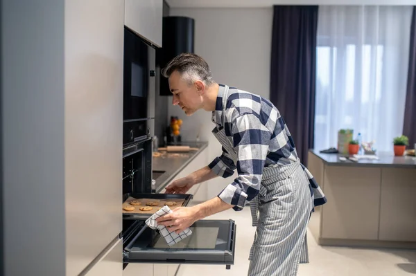 Profile of man putting baking sheet in oven — Fotografia de Stock
