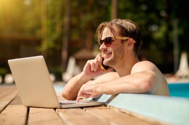 Yüzme havuzundaki genç adam dizüstü bilgisayarla çalışıyor.