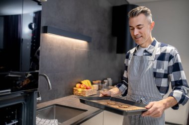 Elinde kurabiye olan bir adam yemek tepsisine bakıyor.