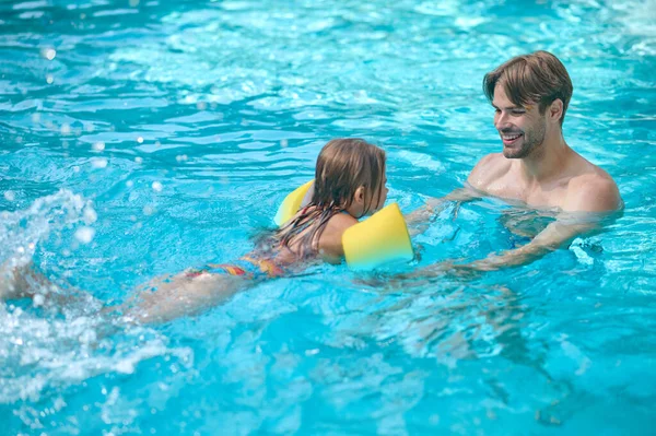 Dad teaching his daughter swimming in a swimming pool — Stock Photo, Image