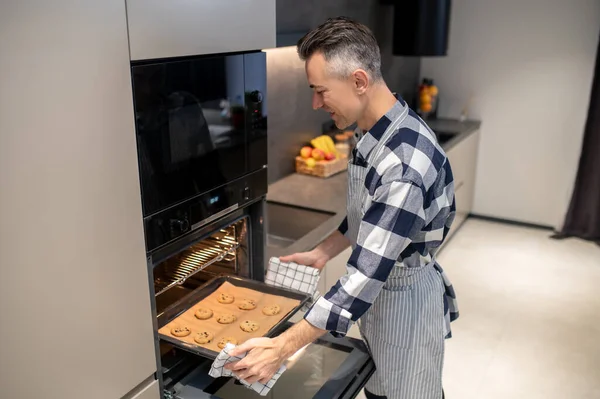 Чоловік дивиться, як завантажується лист для випічки в духовку — стокове фото