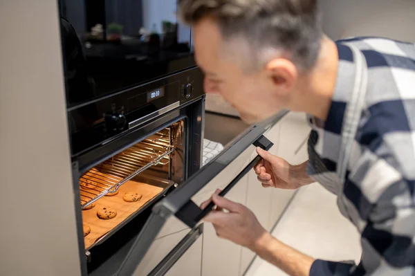 Man op zoek naar open oven bij het bakken koekje — Stockfoto
