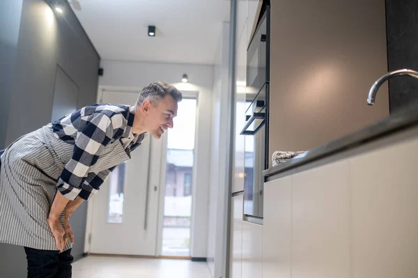 Man sideways to camera leaning towards oven watching — Stock Photo, Image