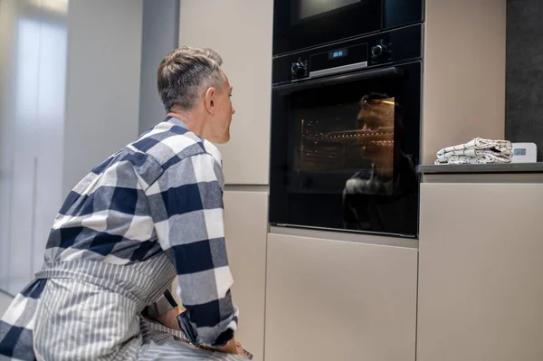 Man crouching near working oven watching — Stock Photo, Image