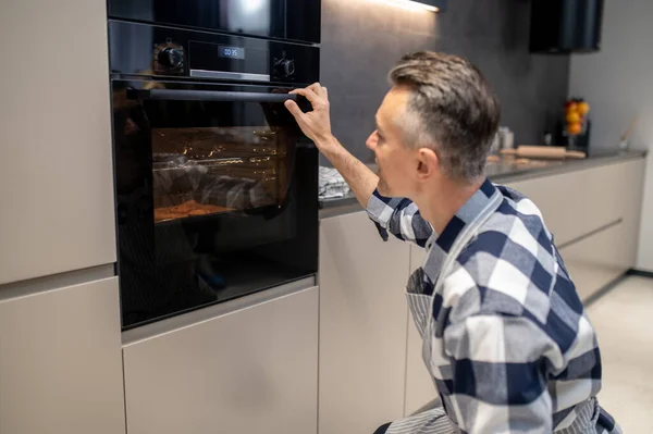 Man hurkt kijken bakken in elektrische oven — Stockfoto