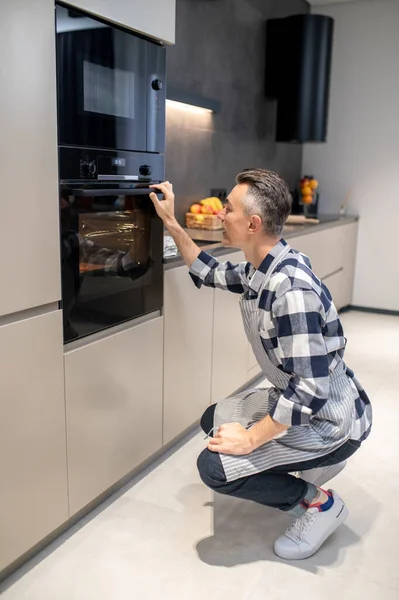 Man crouching near oven touching handle — Stock Photo, Image