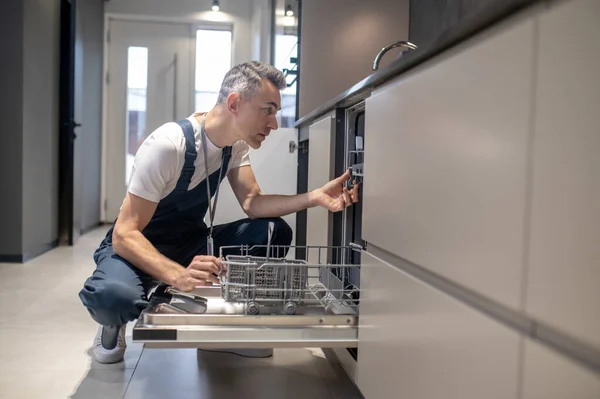 Muž dřepící a kouká do myčky v kuchyni — Stock fotografie