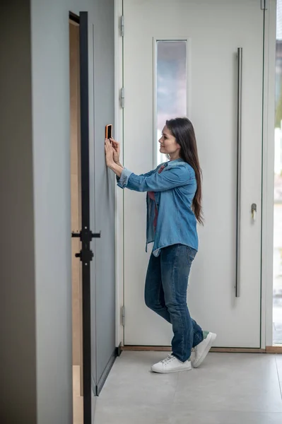 Mujer de pie de lado a la cámara cerca del dispositivo inteligente para el hogar —  Fotos de Stock