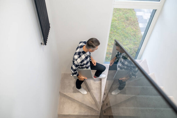 Top view of man with laptop on stairs indoors