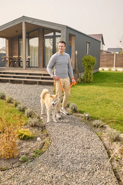 Hombre con perro con correa caminando cerca de casa de campo — Foto de Stock
