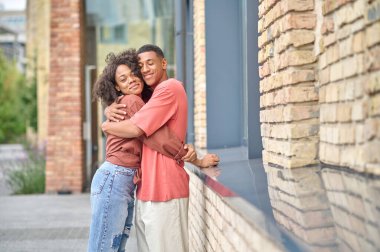 Kapalı gözlü bir adam açık havada kadınlara sarılıyor.