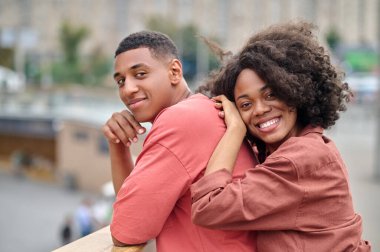 Bir kadın kameraya bakarken erkeğin sırtına dokunuyor.