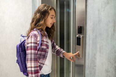 Asansörü çağıran sırt çantalı konsantre genç bayan.