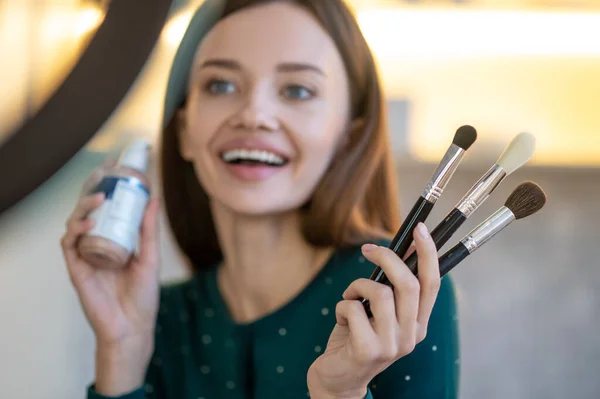 Mujer joven sosteniendo pinceles faciales y sonriendo — Foto de Stock