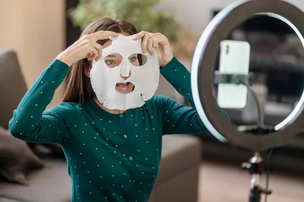 Mujer joven demostrando una máscara hidratante durante el tutorial en línea — Foto de Stock