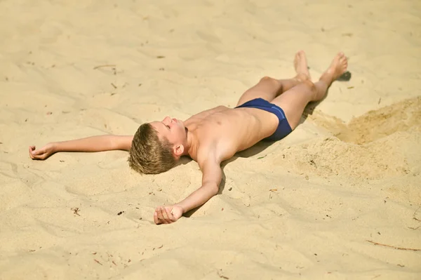 Un garçon bronzant tout allongé sur le sable et l'air détendu — Photo