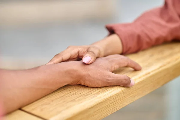 Female hand touching male hand lying on railing — Stock Photo, Image