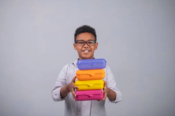 Usmívající se žák demonstrující barevné plastové nádoby na potraviny — Stock fotografie