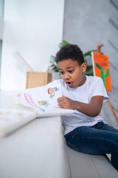 Niño sentado en la habitación mirando libro en sorpresa —  Fotos de Stock