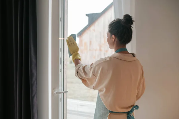Nainen esiliina puhdistus ikkunat ja etsivät mukana — kuvapankkivalokuva
