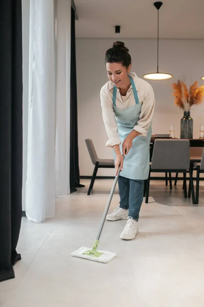 Önlüklü genç bir kadın mutfakta yerleri temizliyor. — Stok fotoğraf
