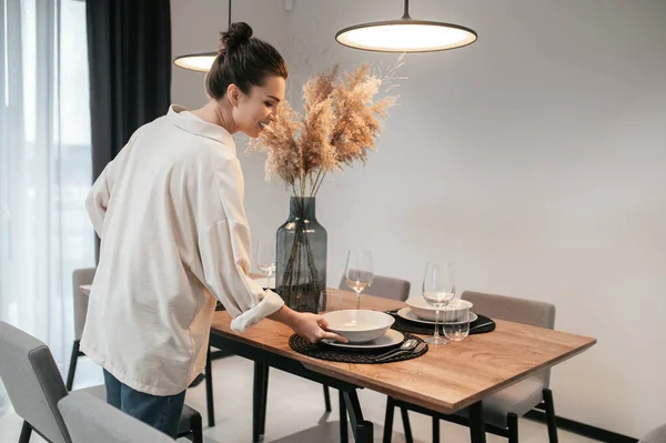 Jovem mulher em uma camisa branca colocando pratos na mesa — Fotografia de Stock