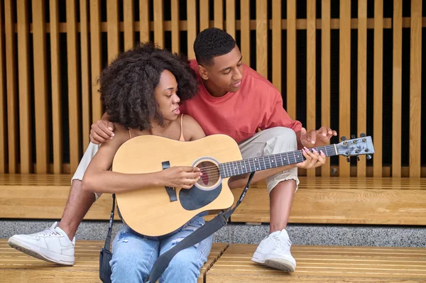 Frau schaut genau auf Saiten von Gitarre und Mann zeigt — Stockfoto