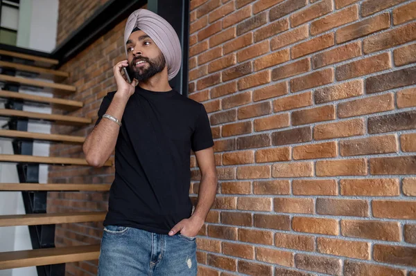 Indian man in beige turban standing on stairs and talking on the phone