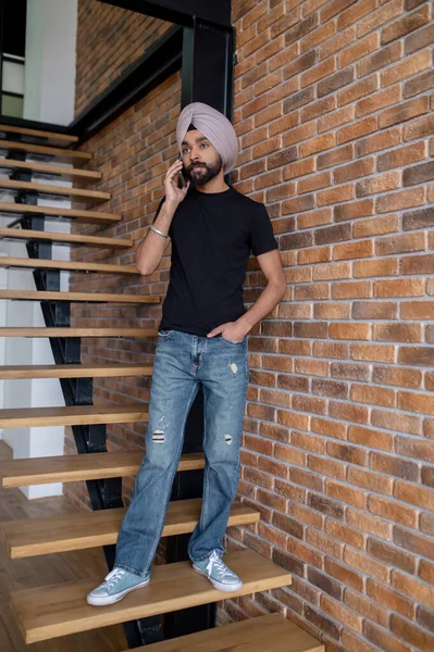 Indian man in beige turban standing on stairs and talking on the phone — Stock Photo, Image