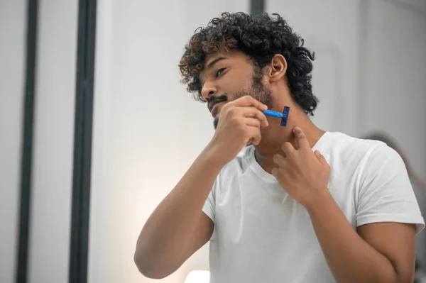 Konzentrierter junger Mann rasiert sich vor dem Spiegel — Stockfoto