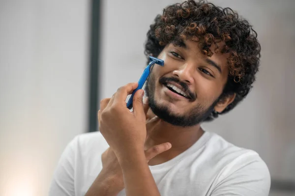 Sonriendo chico complacido quitando el vello facial con una navaja de afeitar de seguridad — Foto de Stock