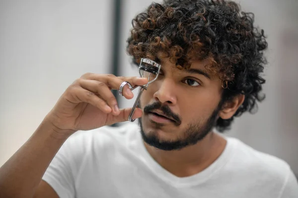 Serious concentrated young man using a lash-curler — Stock Photo, Image