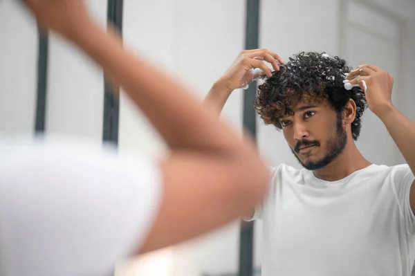 Männchen reibt das Haarstyling-Produkt in seine Locken — Stockfoto