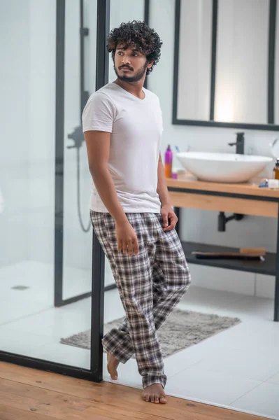 Calm thoughtful curly-haired barefoot male standing in the bathroom doorway — Stock Photo, Image